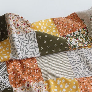 May include: A patchwork fabric featuring a range of floral patterns in shades of yellow, orange, green, and white. The fabric is made from cotton and is ideal for quilting, sewing, and crafting.