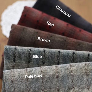 Puede incluir: Muestras de tela en colores carbón, rojo, marrón, azul y azul pálido. Las telas tienen una textura y pequeños puntos oscuros. Los nombres de los colores están escritos en la tela.