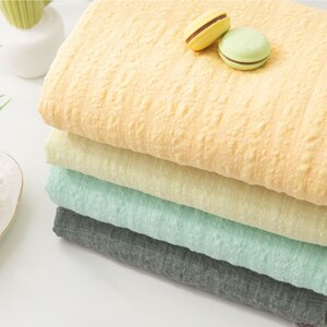 May include: A stack of four fabric swatches in different colors: yellow, light yellow, light green, and gray. The fabric has a textured, crinkled look.
