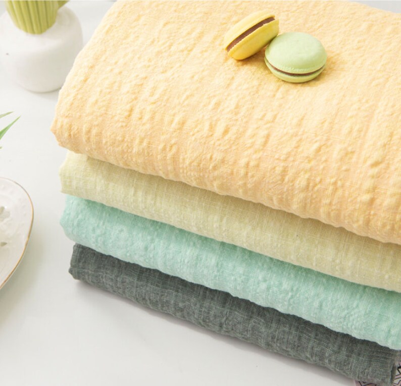 May include: A stack of four fabric swatches in different colors: yellow, light yellow, light green, and gray. The fabric has a textured, crinkled look.