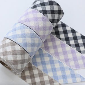 May include: A selection of gingham patterned ribbons in a range of colours, including black and white, lilac, pale blue, and brown. The ribbons are rolled and partially unrolled, displaying the fabric's texture. Each ribbon has a classic check design.