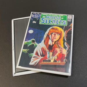 May include: A vintage comic book cover featuring a woman in a white robe with red accents, looking frightened. The cover is titled "The House of Secrets" and features a green monster in the background. The comic book is from DC Comics and costs 15 cents.