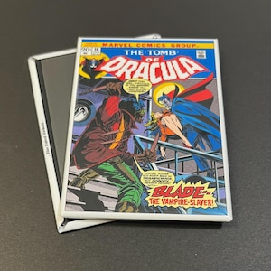 May include: A vintage comic book cover featuring a black and green character with a red shirt and a red and blue character with a cape. The comic book cover is titled "The Tomb of Dracula" and features the text "Blade: The Vampire-Slayer!"