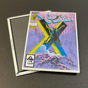 May include: A vintage comic book cover featuring the X-Men. The cover is white with a yellow and blue X in the center. The title "The Uncanny X-Men" is printed in black and red letters. The cover features a black and white illustration of a superhero with a yellow and blue X behind them.