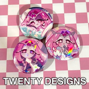 May include: Three round, colorful buttons with anime-style character designs in shades of pink, purple, and white. The buttons feature holographic accents and the text "TWENTY DESIGNS" in white. The background is a pink and white checkered pattern.