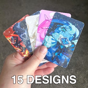 May include: A hand holding a fan of five colorful cards with cartoon character designs. The cards feature various colors, including red, blue, pink, and white. The text "15 DESIGNS" is at the bottom.
