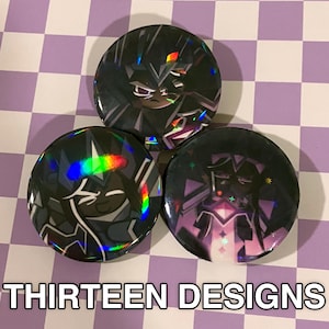 May include: Three round, black and iridescent buttons with character designs. The buttons have a holographic effect, with the text "THIRTEEN DESIGNS" at the bottom. The background is a purple and white checkered pattern.