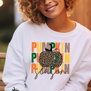Può includere: Felpa bianca con un design grafico di una zucca con stampa leopardata con il testo "Pumpkin Season" in lettere colorate impilate.