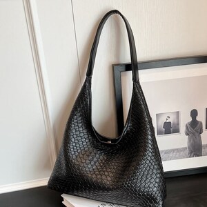May include: Black woven leather shoulder bag with a single strap. The bag has a slouchy, relaxed shape.