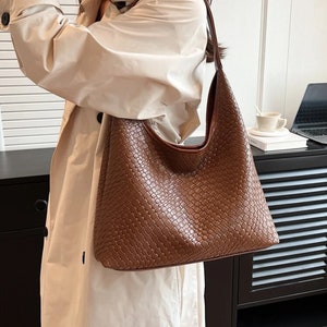 May include: A brown woven leather shoulder bag with a long strap. The bag has a slouchy, casual style.