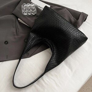 May include: A black woven tote bag with a single strap. The bag has a textured, woven design.