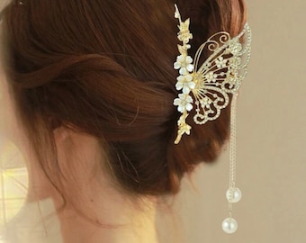 May include: A gold butterfly hair comb with white pearl accents and a dangling pearl chain. The comb is decorated with rhinestones and small white flowers.