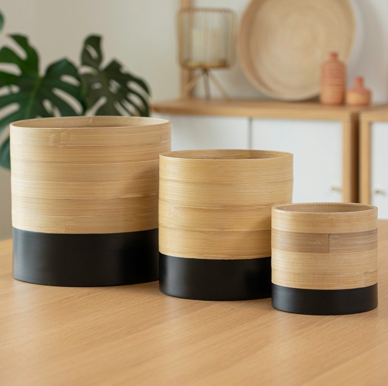 May include: Three round bamboo planters with black bottoms. The planters are different sizes and are arranged from largest to smallest.