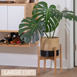 May include: A large, 10-inch diameter, black and natural bamboo planter with a monstera plant. The planter sits on a wooden stand with four legs.