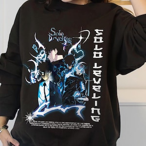 Puede incluir: Sudadera negra con un estampado gráfico de personajes del anime "Solo Leveling". El texto "Solo Leveling" está impreso verticalmente en el lado derecho del gráfico. El texto "Solo Developing" está impreso encima del gráfico.