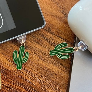 May include: Four gold cactus charms with green cactus designs attached to a tablet and a white case. A gold key chain with a gold clasp is also included.