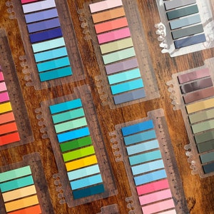 May include: A set of colorful sticky note tabs with a ruler on the side. The tabs are arranged in rows of different colors, including pink, blue, green, yellow, and orange. The tabs are perfect for marking pages in books, journals, and planners.