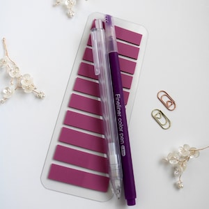 Pinkish Purple annoation tab sheet with one transparent mechanical pencil, one blue felt tip pen and two mini paper clip (gold and rose gold) on a white surface. This elementas are part of the mini kit offering. Annotation tab pallet is lilac bliss.