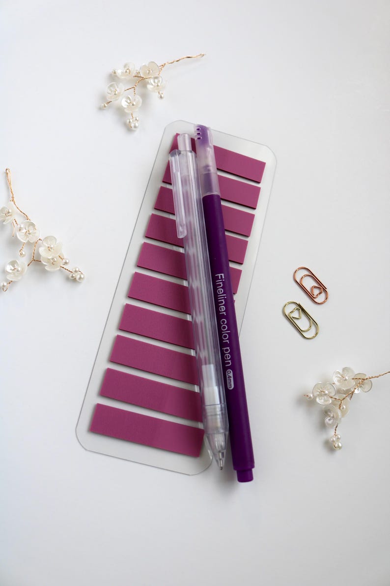 Pinkish Purple annoation tab sheet with one transparent mechanical pencil, one blue felt tip pen and two mini paper clip (gold and rose gold) on a white surface. This elementas are part of the mini kit offering. Annotation tab pallet is lilac bliss.