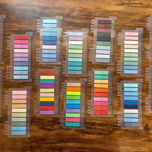 May include: A set of 15 color swatches, each with 10 different shades of color. The swatches are arranged in rows on a wooden surface. The colors include shades of blue, green, yellow, orange, red, purple, pink, and brown.