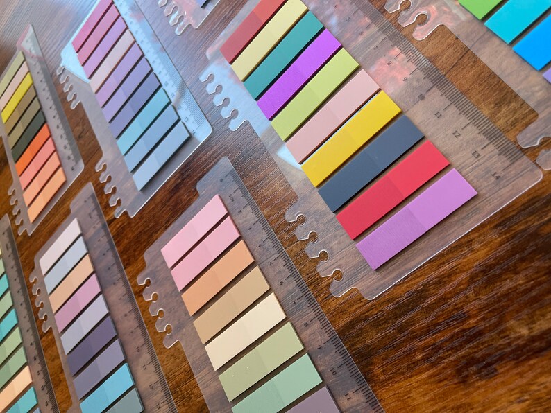 May include: A set of colorful sticky notes with a ruler on each sheet. The notes are arranged in rows of different colors, including pink, orange, yellow, green, blue, purple, and red.