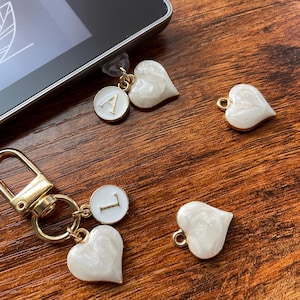 May include: Two white heart-shaped charms with gold accents and a gold letter charm with the letter 'A' on a white background. Two more white heart-shaped charms with gold accents and a gold letter charm with the letter 'L' on a white background.