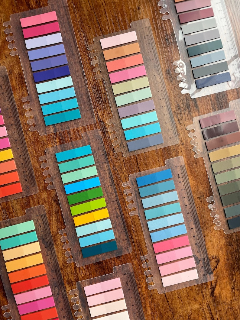 May include: A set of colorful sticky note tabs with a ruler on the side. The tabs are arranged in rows of different colors, including pink, blue, green, yellow, and orange. The tabs are perfect for marking pages in books, journals, and planners.