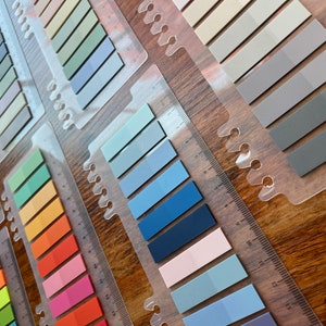 May include: A set of colorful sticky notes in various shades of blue, green, yellow, orange, pink, and red. The notes are arranged in rows on a clear plastic holder with a ruler.