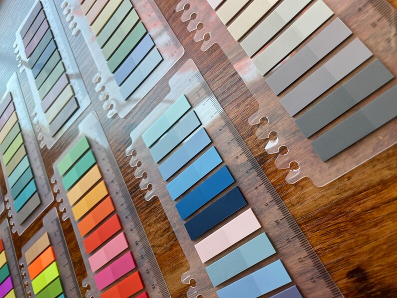 May include: A set of colorful sticky notes in various shades of blue, green, yellow, orange, pink, and red. The notes are arranged in rows on a clear plastic holder with a ruler.