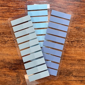May include: Three sheets of clear adhesive note tabs with blue and gray stripes. The tabs are arranged vertically, with the blue tabs on the left and right, and the gray tabs in the middle.