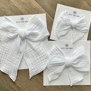 May include: Three white fabric bows of varying sizes on white card stock with the text "Daisy Lane Bows" printed on each card.
