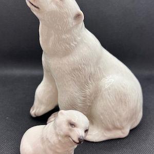 Könnte beinhalten: Eine weiße Porzellanfigur einer Eisbärin mit ihrem Jungen. Die Mutter sitzt aufrecht mit erhobenem Kopf, während das Junge vor ihr sitzt und den Betrachter ansieht.