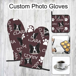 Puede incluir: Un par de guantes de horno marrones con una huella de pata blanca y un patrón de cara de perro blanco y negro. Los guantes tienen el nombre "Clara" impreso en ellos.