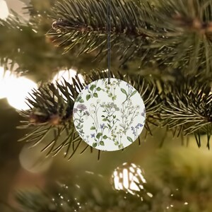 May include: A round white bauble with a floral pattern featuring small white and purple flowers and green leaves.
