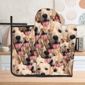May include: A pair of oven mitts with a pattern of multiple golden retriever dog faces. The mitts are black with a white trim.