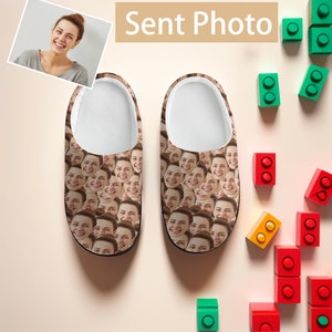 May include: A pair of brown slippers with a pattern of many faces. The slippers are on a white background with colourful toy blocks.