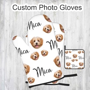 May include: A set of two white oven mitts and a matching pot holder with a repeating pattern of a dog's face and the name "Mica" printed in black.