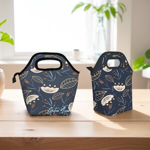 Könnte beinhalten: Zwei isolierte Lunch-Taschen mit einem Blumenmuster. Die größere Tasche hat einen schwarzen Griff und den Text "Custom Name" auf der Vorderseite. Die kleinere Tasche hat einen Reißverschluss.