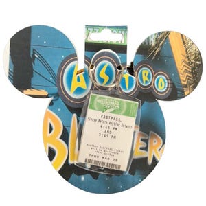 May include: A Buzz Lightyear Astro Blasters Fastpass ticket on a Mickey Mouse-shaped keychain. The ticket is in a clear plastic holder and has text that reads "Please Return Anytime Between 4:45 PM AND 5:45 PM". The background is blue with star and space-themed graphics.