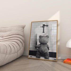Black and white novelty wall art featuring a teddy bear drinking beer in a humorous bathroom setting.