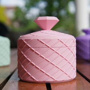 Pode incluir: Quatro recipientes decorativos com tampas em forma de diamante. Os recipientes são feitos de um material texturizado e são em tons de rosa, verde, roxo e branco.