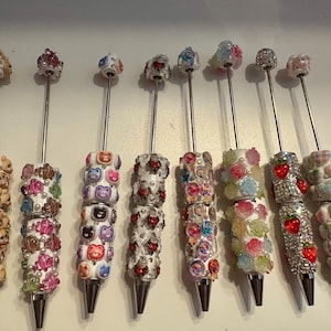 May include: A selection of decorative bottle stoppers. Each stopper has a silver stem and a decorative top. Designs include bears, flowers, strawberries, and other colourful embellishments. These stoppers are suitable for wine bottles.