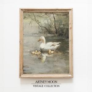 May include: A framed vintage painting shows a white duck and its ducklings in a pond. The artwork has a muted colour palette and a light brown wooden frame. The text "ARTNEY MOON VINTAGE COLLECTION" is at the bottom of the painting.