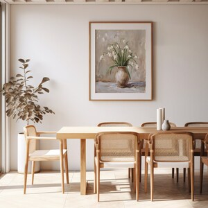 May include: A framed painting of a white flower bouquet in a brown vase, hanging on a white wall above a wooden dining table with six chairs.