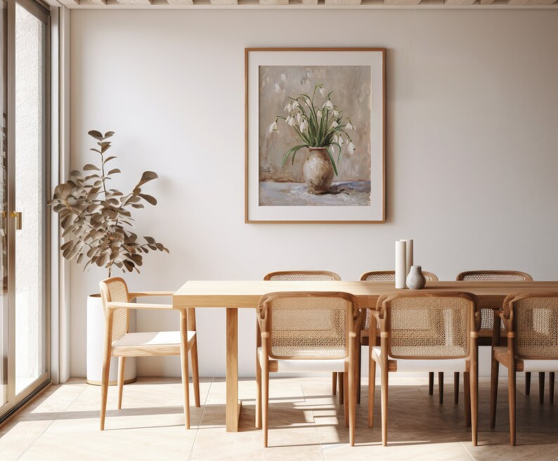 May include: A framed painting of a white flower bouquet in a brown vase, hanging on a white wall above a wooden dining table with six chairs.