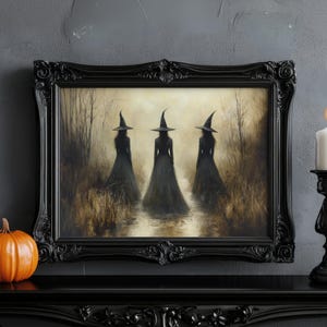 May include: A black framed print of three witches wearing black pointed hats and long black dresses walking through a forest. The print is set against a gray wall with a black candle holder and a pumpkin in the foreground.