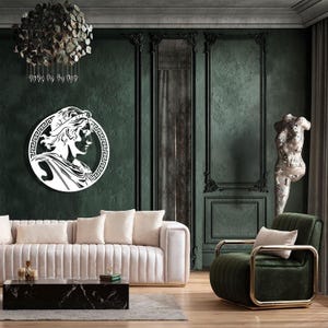 May include: A white silhouette of a person's head with a crown on a dark green wall with ornate moulding. The silhouette is inside a circle with a Greek key design. A white sofa with a black marble coffee table is in the foreground. A green velvet armchair with gold accents is in the right corner of the image.