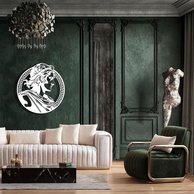 May include: A white silhouette of a person's head with a crown on a dark green wall with ornate moulding. The silhouette is inside a circle with a Greek key design. A white sofa with a black marble coffee table is in the foreground. A green velvet armchair with gold accents is in the right corner of the image.