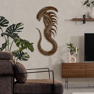 May include: A brown wall decor featuring a stylized alien creature with a long tail and sharp teeth. The alien is in a curled position, with its head tilted down. The decor is mounted on a light brown wall.
