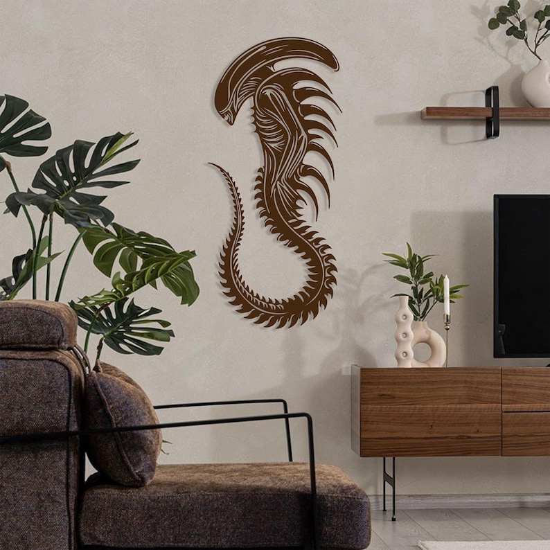 May include: A brown wall decor featuring a stylized alien creature with a long tail and sharp teeth. The alien is in a curled position, with its head tilted down. The decor is mounted on a light brown wall.